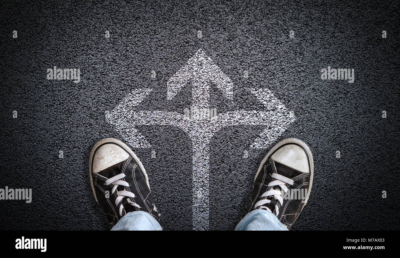 Ein Teenager in Jeans und Canvas Schuhe stehen auf Asphalt mit 3-Wege-Pfeil in der Mitte und Kopieren. Konzept der ständigen an der Kreuzung Stockfoto