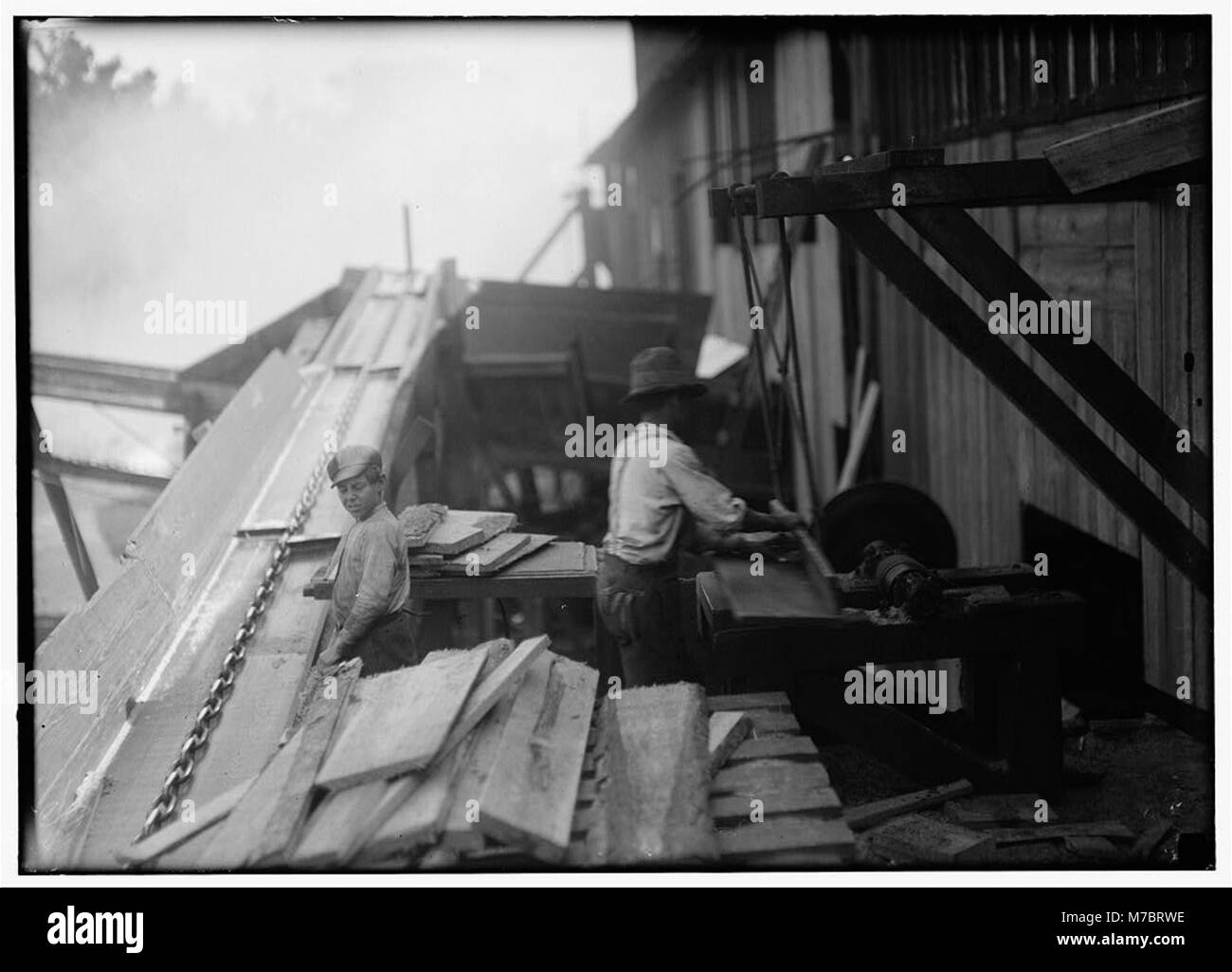 Charlie McBride, ein 12-jähriger Junge, wird gezeigt, wie er bei der Miller and Vidor Lumber Company arbeitet, indem er Platten von einem beweglichen Rutschkorb aus bearbeitet, was die Gefährlichkeit der Kinderarbeit im frühen 20. Jahrhundert demonstriert. Stockfoto