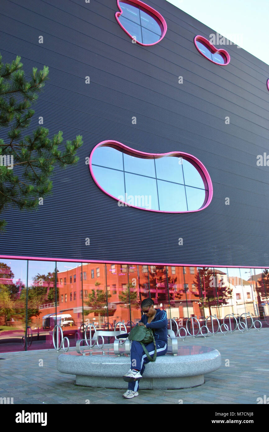 Schwarze Dame sitzen auf einer Bank vor der Öffentlichkeit durch Will Alsop, jetzt Teil von Sandwell College, West Bromwich Stockfoto