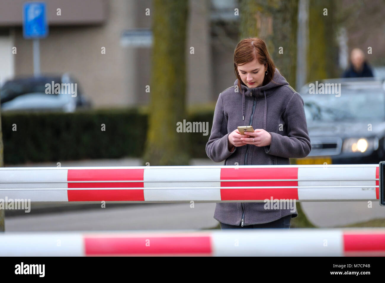 Junge Frau besetzt ist, auf Ihr Handy vor einer Bahn Übergang mit Schranken geschlossen Stockfoto