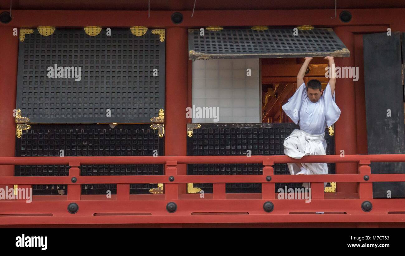 Shinto Priester in weißen Gewändern auf tsurugaoka Hachimangū schrein Geländer schließen große hölzerne Fenster in Vorbereitung der Schließung gekleidet. Stockfoto