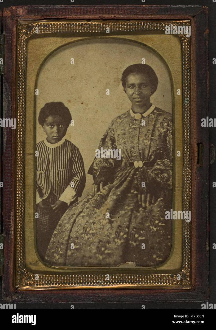 Dieses Porträt zeigt eine nicht identifizierte Frau, die neben ihr ein Kind steht. Beide Figuren stehen vor der Kamera und bieten einen klaren Einblick in ihr Aussehen und ihre Kleidung aus dem frühen 20. Jahrhundert. Stockfoto