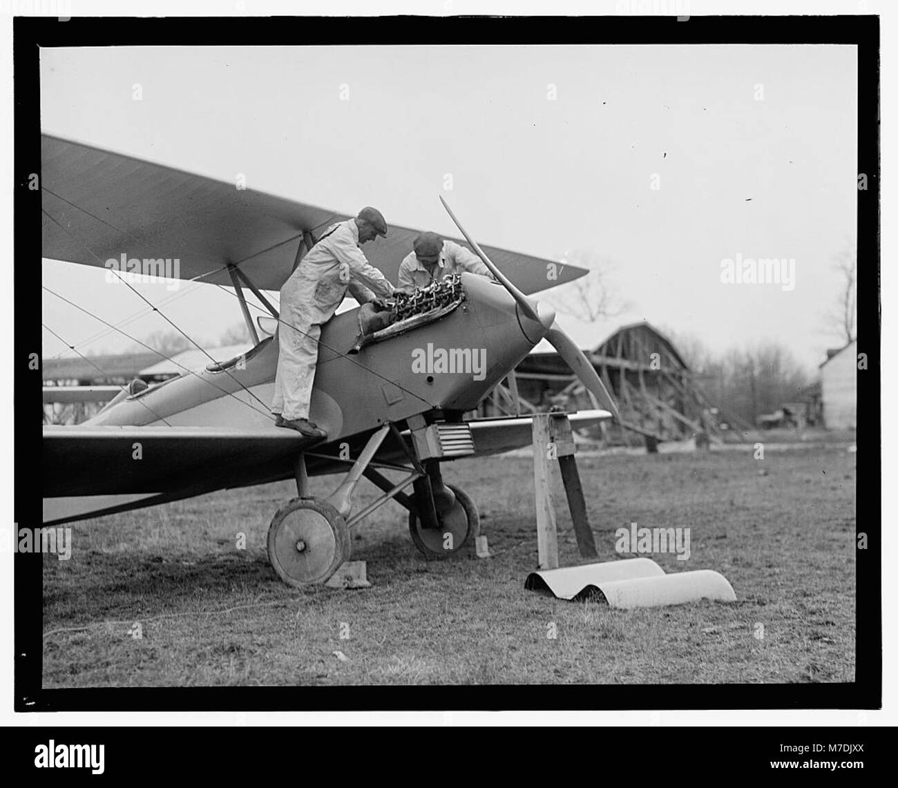 Dieses Foto zeigt Männer, die einen Flugzeugmotor untersuchen, möglicherweise für Wartung oder Inspektion, was die technischen Aspekte der frühen Luftfahrt widerspiegelt. Stockfoto