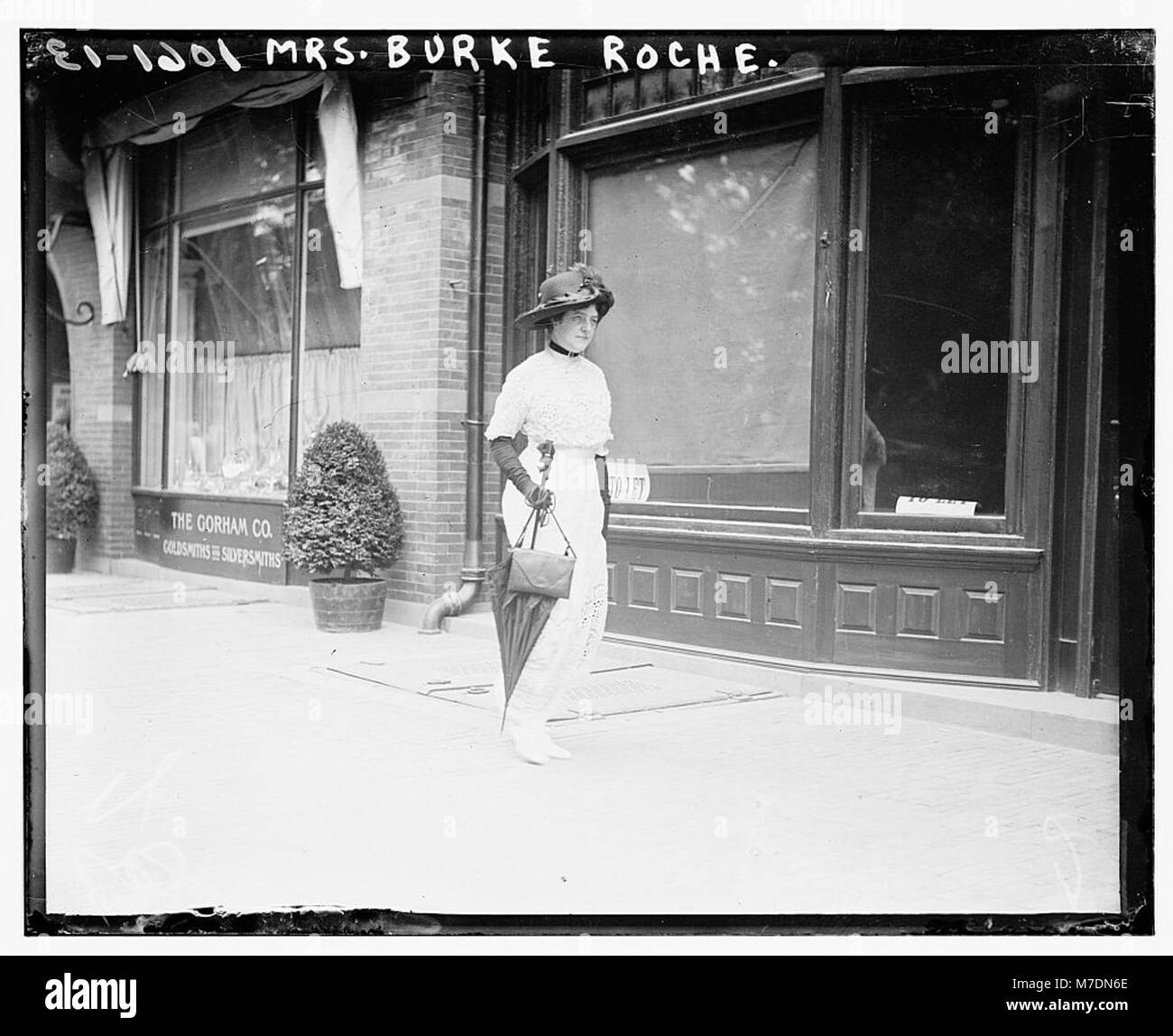 Dieses Foto zeigt Mrs. Burke Roche auf einem Bürgersteig mit Sonnenschirm, wahrscheinlich in einer modischen Umgebung aus dem 19. Jahrhundert. Das Bild spiegelt die Kleidung und sozialen Normen der Zeit wider. Stockfoto