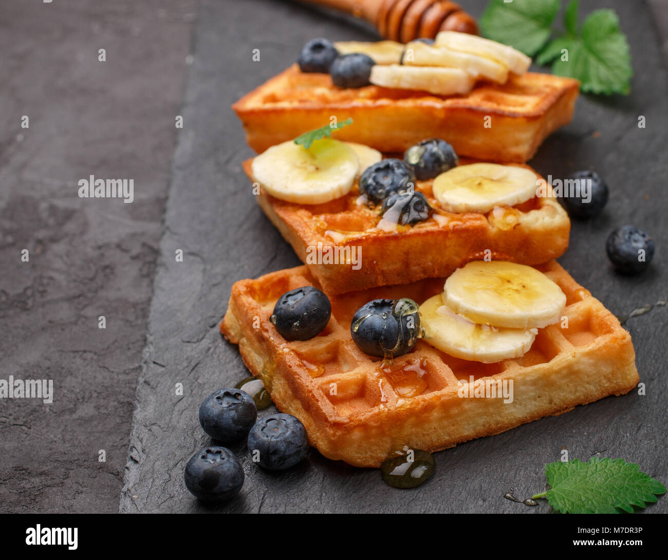 Traditionelle belgische Waffeln mit Blaubeeren, Banane und Honig auf schwarzem Schiefer Platte. Gourmet Frühstück. Selektiver Fokus Stockfoto