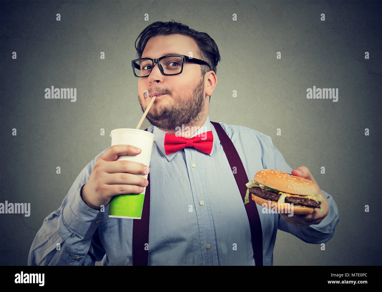 Junge chunky Mann in formalen Outfit mit Soda und Hamburger auf grauen Hintergrund. Stockfoto