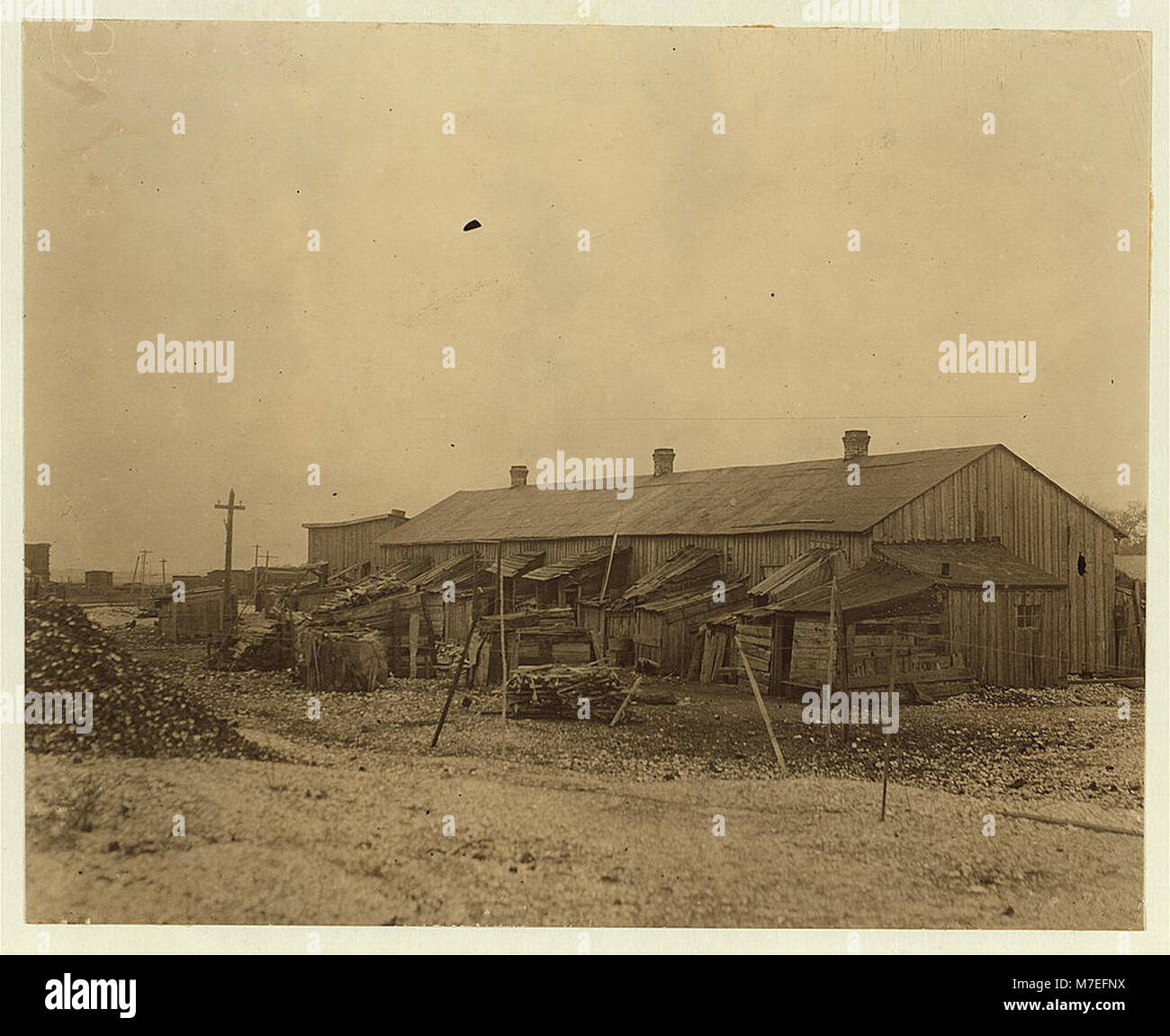 Eine Fotografie von 50 Menschen, die in baufälligen Hütten auf einem Muschelhaufen in der Nähe eines Gezeitenmoors leben, die schlechte Lebensbedingungen und die sozialen Probleme der damaligen Zeit widerspiegeln, die wahrscheinlich mit wirtschaftlichen Schwierigkeiten oder Arbeitslagern in Verbindung stehen. Stockfoto