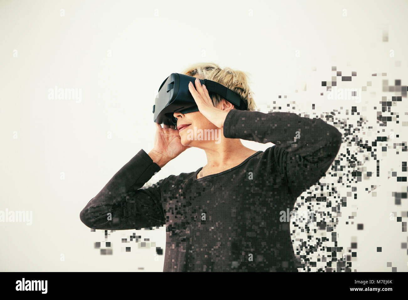 Eine ältere Frau in virtual reality Brillen ist durch Pixel verteilt. Konzeptionelle Fotografie mit visuellen Effekten mit einer älteren Person mit moderner Technologie. Stockfoto