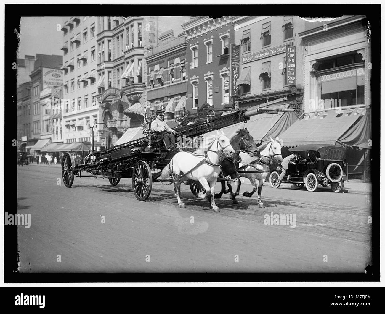 Ein historisches Foto zeigt einen Feuerwehrwagen mit drei Pferden und einem Wasserturm, der den 1300 Block der F Street in Washington, D.C. passiert. Das Studio Harris & Ewing ist über dem Kopf des Fahrers zu sehen. Das Bild zeigt einen wichtigen Moment der Feuerlöschausrüstung in der Stadt. Stockfoto