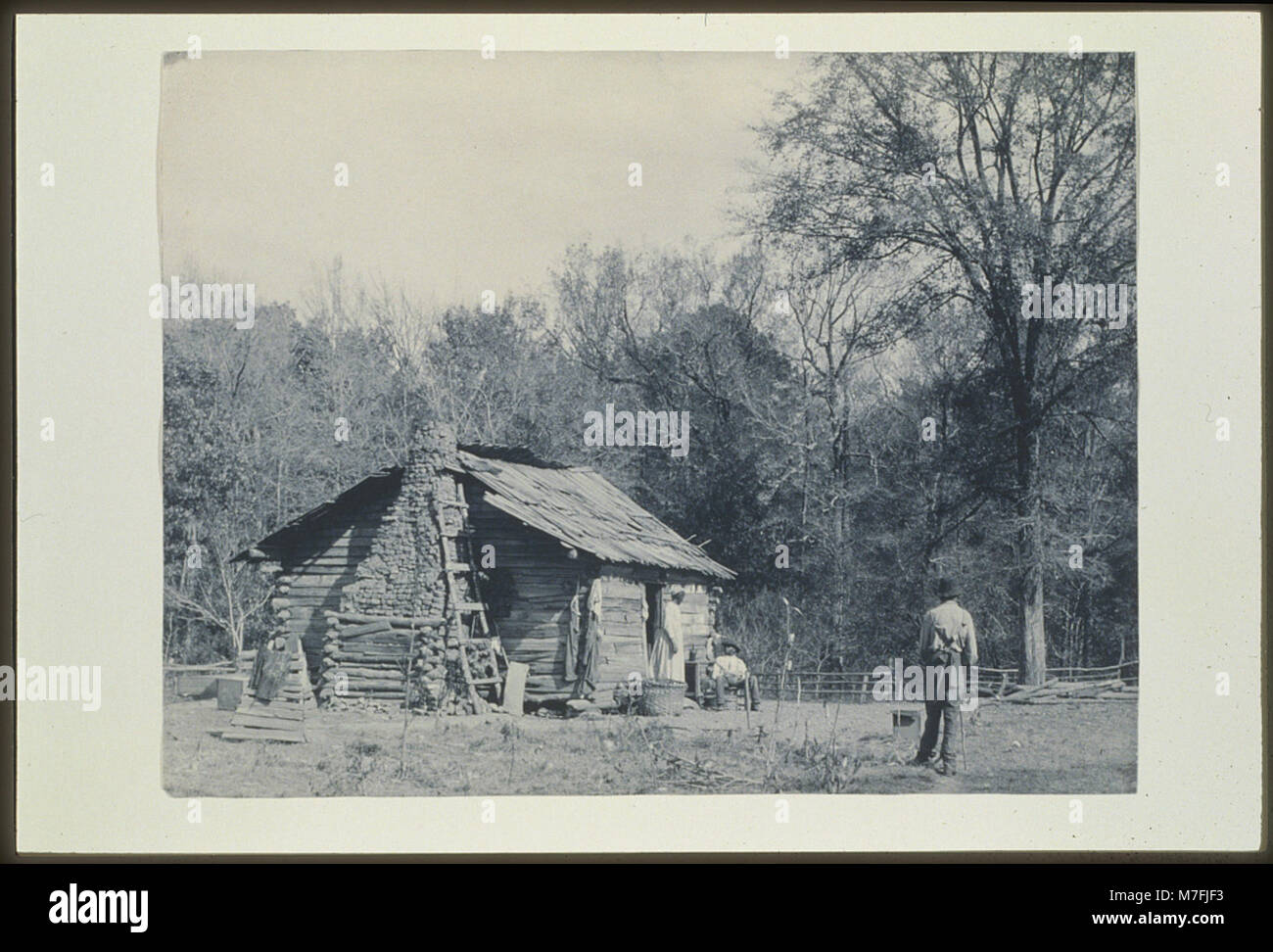 Drei afroamerikanische Personen stehen vor einer Hütte, möglicherweise in Mt. Meigs, Alabama, spiegelt das ländliche Leben im Süden der USA während des frühen 20. Jahrhunderts wider. Stockfoto