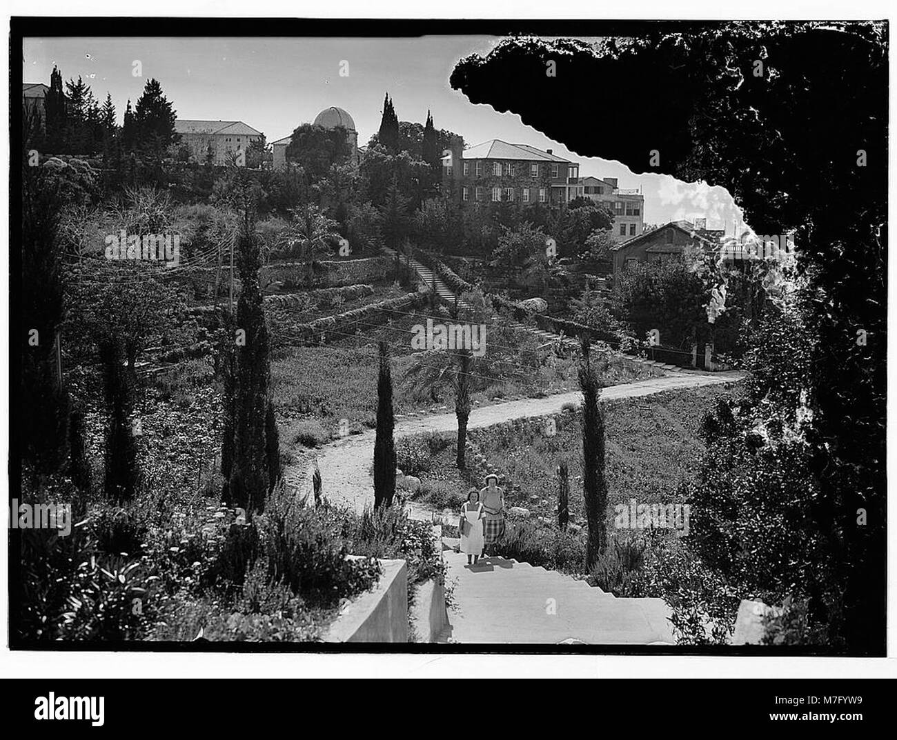 Ein Foto von Frauen, die auf einem Pfad mit Gebäuden im Hintergrund an der Amerikanischen Universität in Beirut spazieren, das den Alltag und die Bildungsumgebung des frühen 20. Jahrhunderts darstellt. Stockfoto