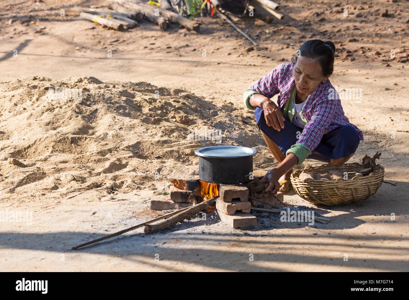 Lokale Frau mit Pan auf offenem Feuer kochen außerhalb in Bagan, Myanmar (Birma), Asien im Februar Stockfoto