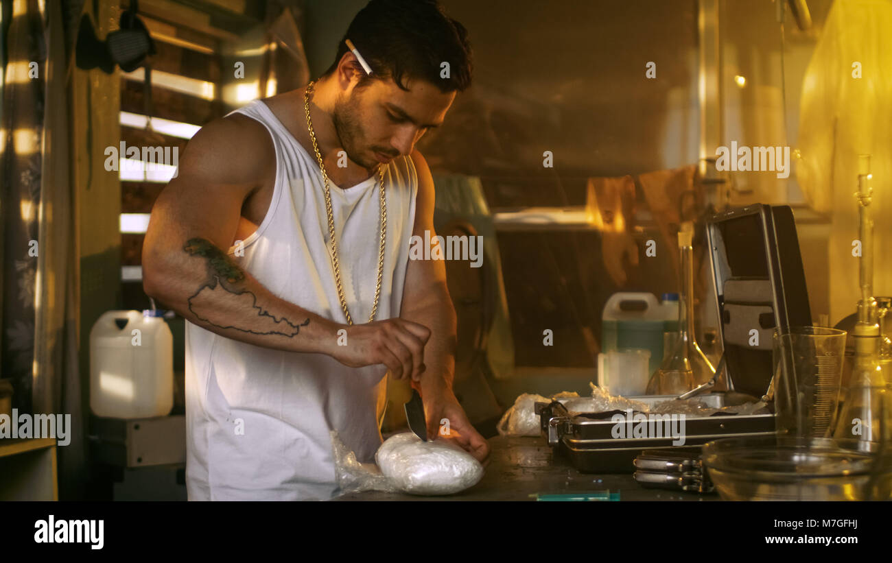 Brutale Drogendealer nimmt Droge Ziegel aus dem Koffer und schneidet ihn mit einem Messer gepackt, eine Probe zu versuchen. Er hockt in das verlassene Gebäude. Stockfoto