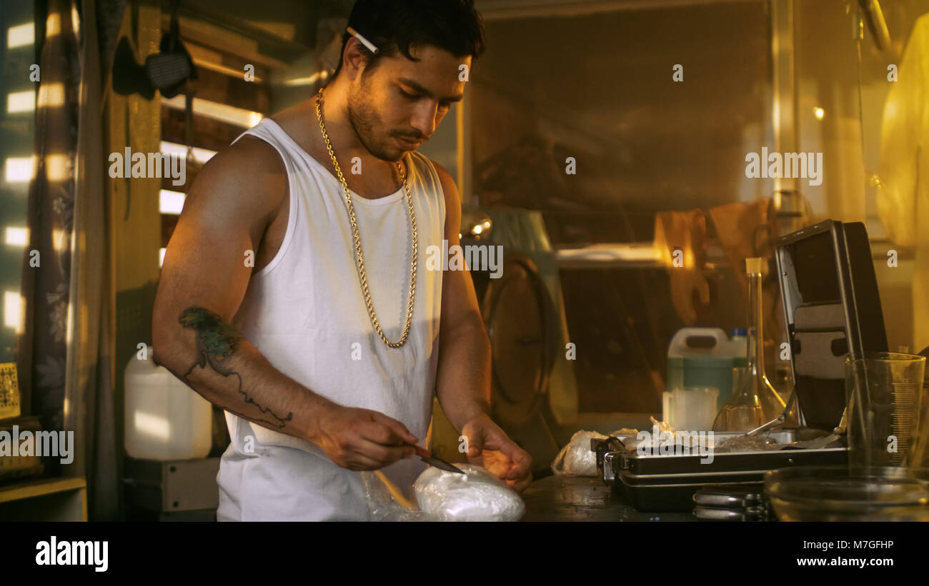 Brutale Drogendealer nimmt Droge Ziegel aus dem Koffer und schneidet ihn mit einem Messer gepackt, eine Probe zu versuchen. Er hockt in das verlassene Gebäude. Stockfoto