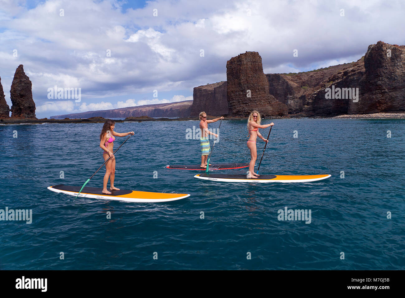 Drei junge Leute auf Stand-up Paddle Boards an Nadeln vor der Insel Lanai, Hawaii. Alle drei sind Model Released. Stockfoto