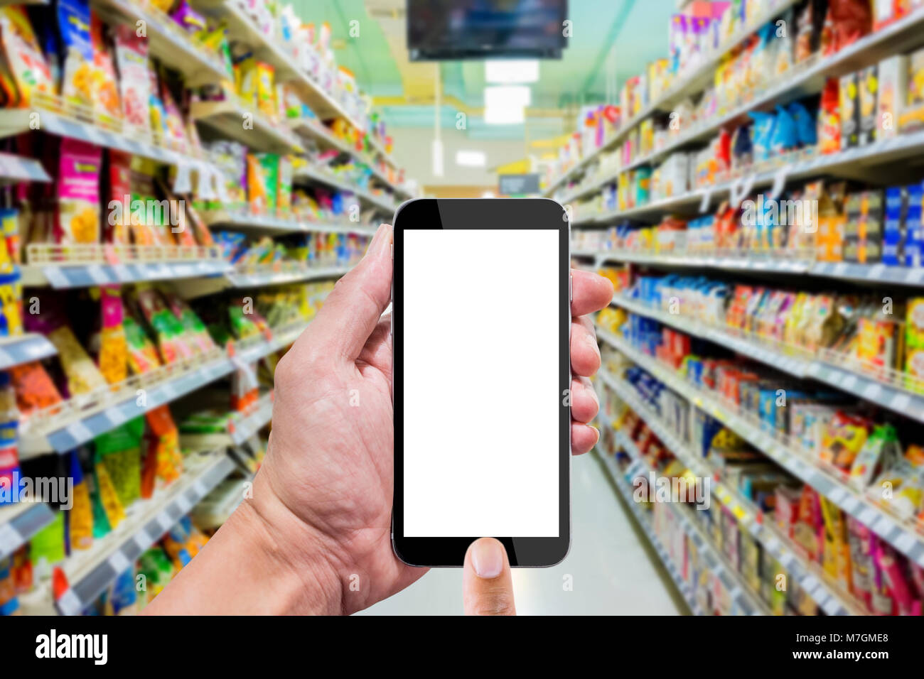 Mit Smartphone in supermartket. Snacks in den Regalen im Gang. Stockfoto