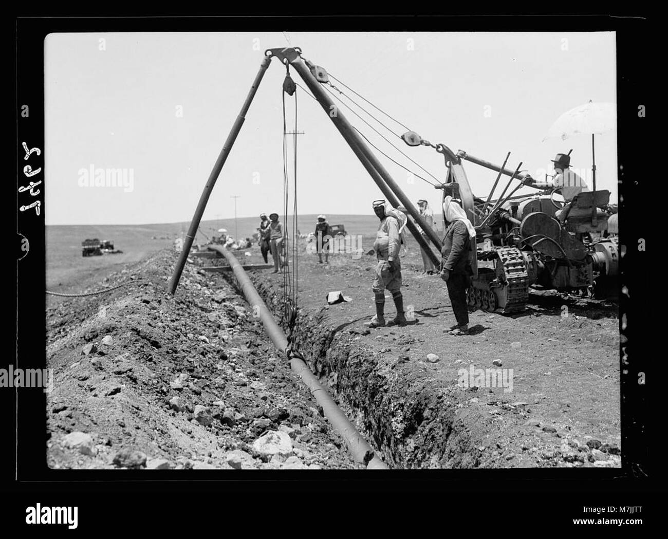Ein Bild, das eine Arbeitsszene bei der Iraq Petroleum Company (IPC) im Esdraelon Valley zeigt, wie Arbeiter im Rahmen des Baus einer Ölpipeline ein Rohr in einen Graben fallen lassen und kurbeln. Das Bild zeigt die industrielle Arbeit im Nahen Osten während des frühen 20. Jahrhunderts. Stockfoto