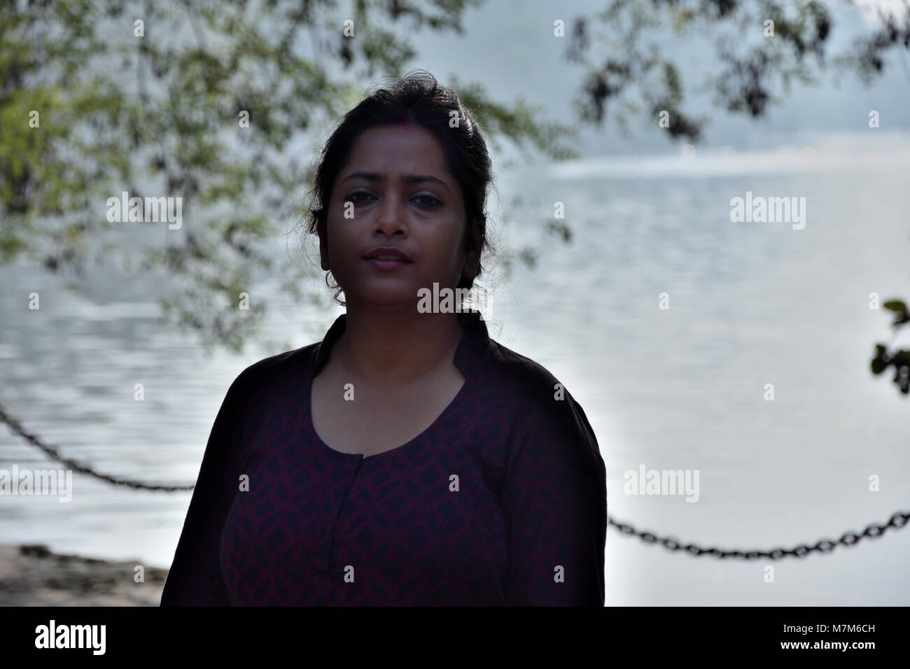 Schöne bengali Mädchen steht vor einem See unter dem Schatten eines Baumes. Stockfoto