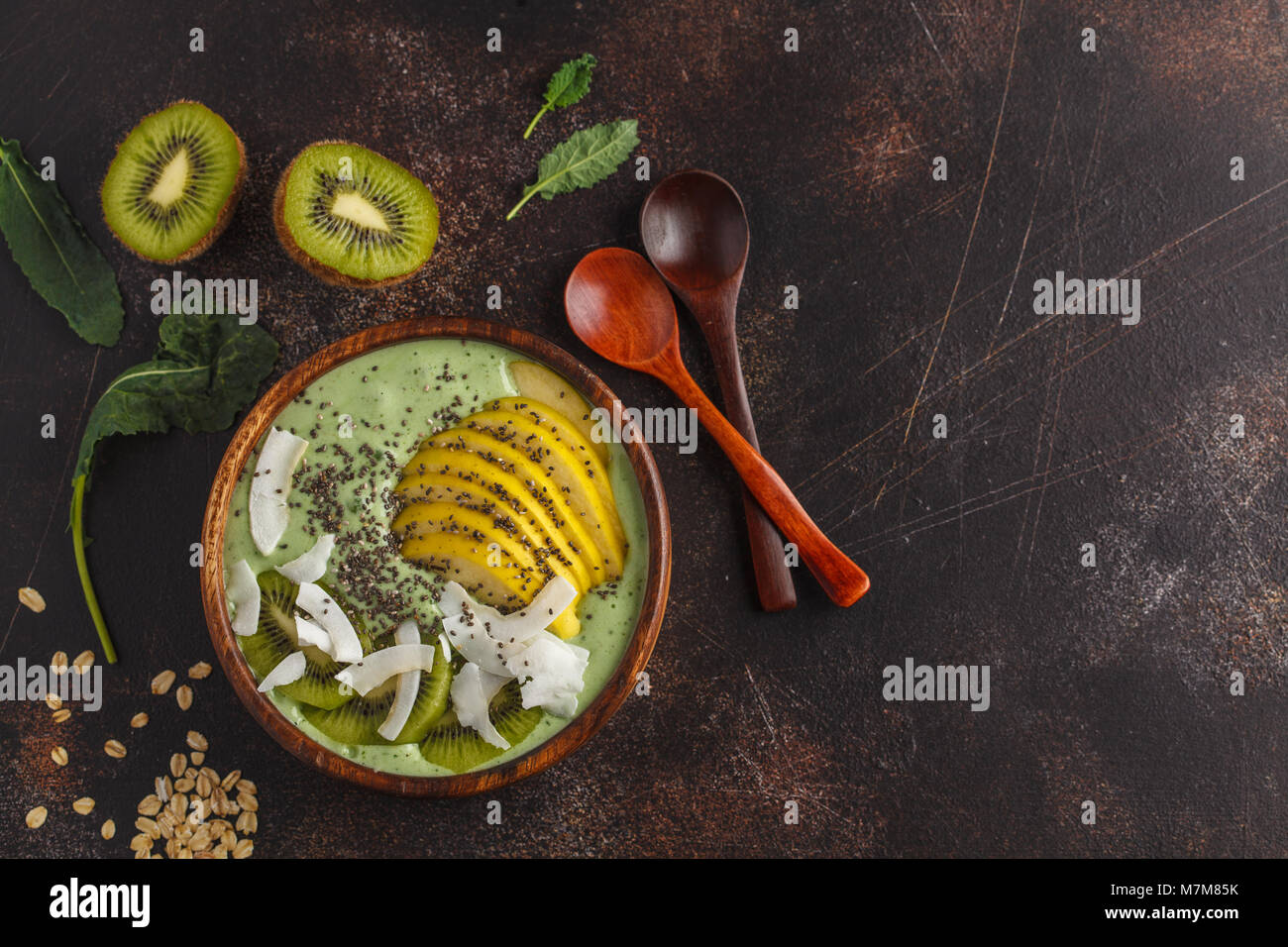 Grünkohl vegan Smoothie Schüssel mit Kokosnuss, Chia, Apple und Kiwi. Gesunde vegane Ernährung Konzept. Dunkle Rusty Hintergrund, Ansicht von oben Stockfoto