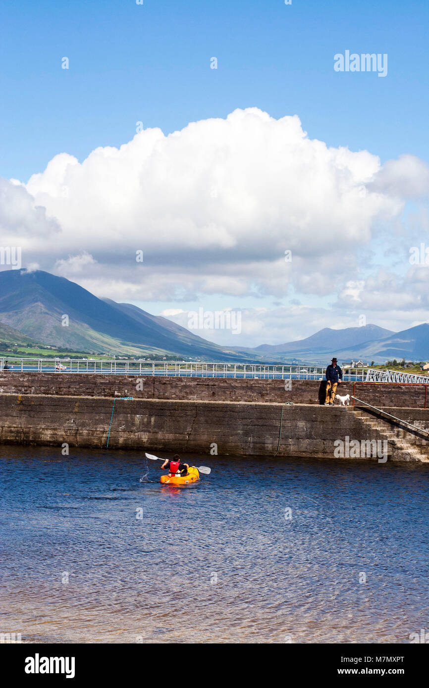 Mann, der seinen Hund am Ende der Pier, Hafenmauer, orange Kanu, vor einer atemberaubenden Landschaft Hintergrund, Ring of Kerry Kerry Irland Stockfoto