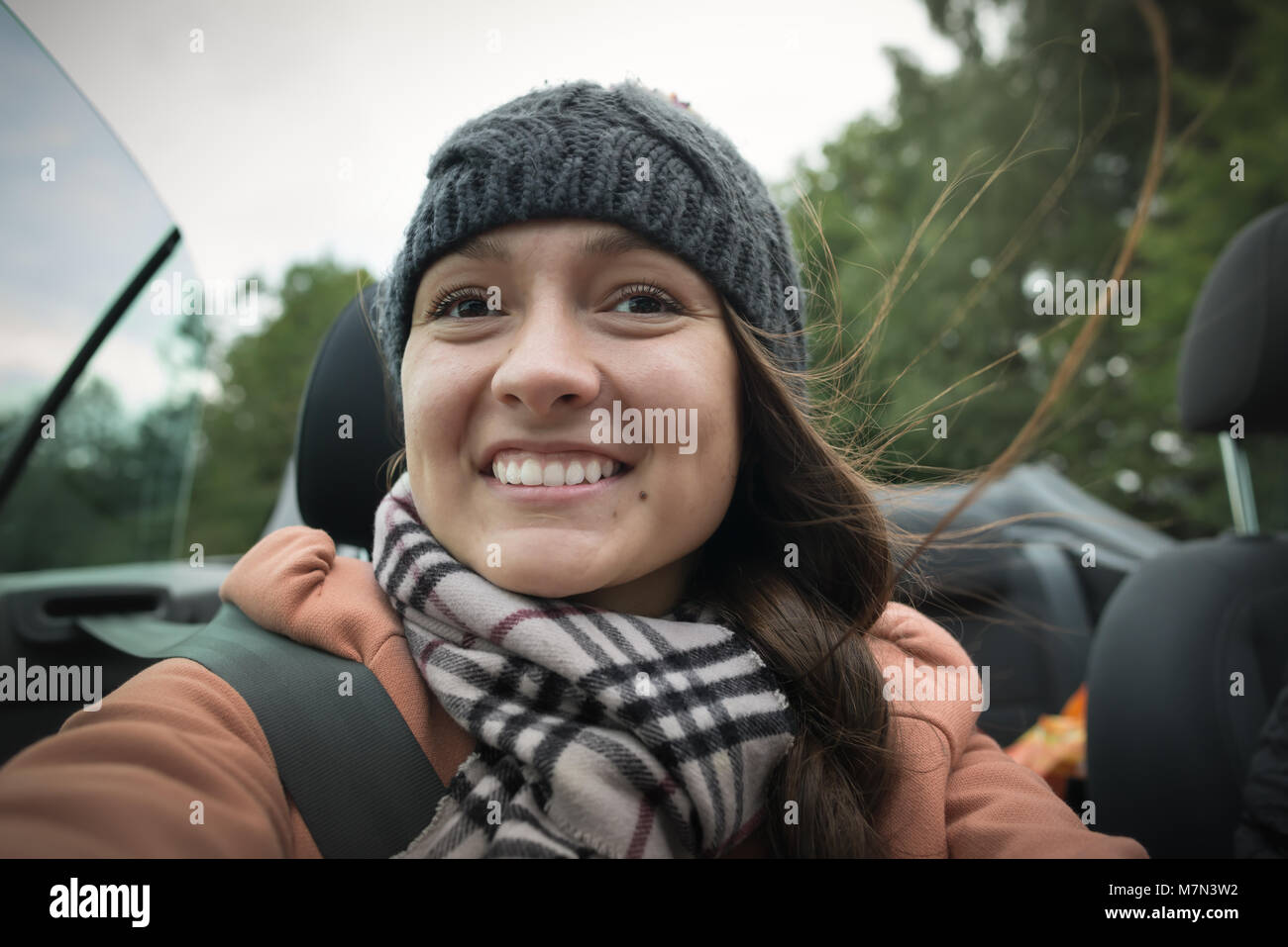 Eine junge fröhliche Mädchen ist unterwegs im Cabrio Auto. Close-up von vorne: lächelnd weibliche Gesicht auf Hintergrund der Himmel und Bäumen. Off-road Abenteuer Stockfoto