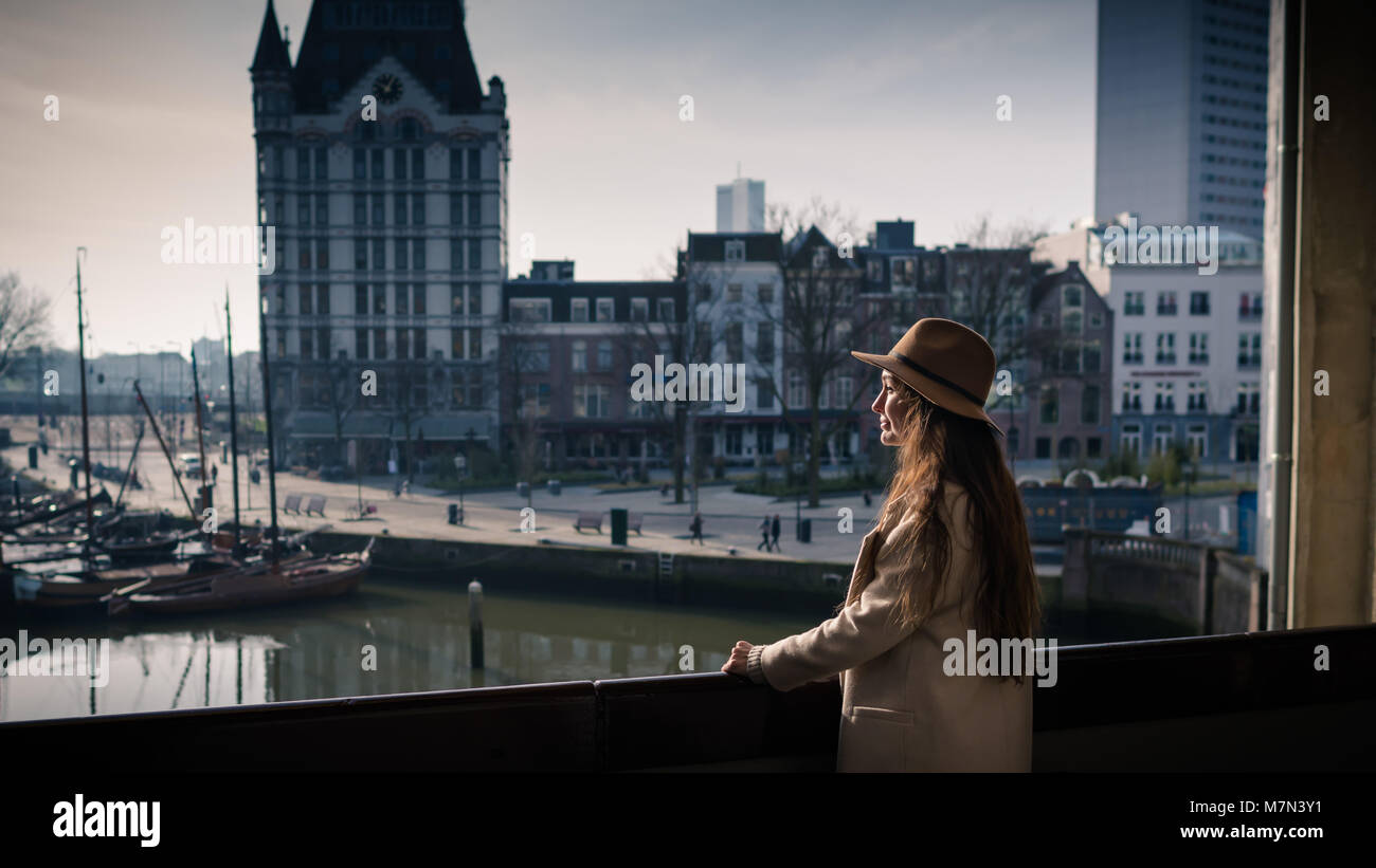 Junge Frau steht auf dem Balkon, in der Nähe des Alten Hafen und in die Innenstadt von Rotterdam, Niederlande. Elegante Hündin touristische Stadt in sonniger Tag erkunden. Stockfoto