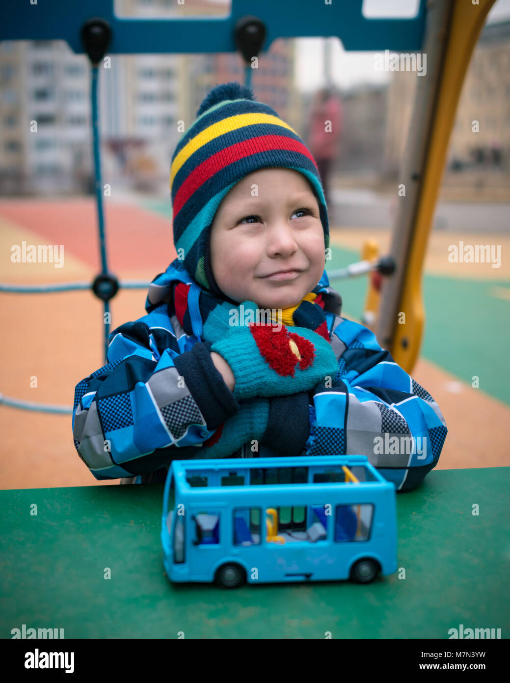 Schönes Kind auf dem Spielplatz im Winter. Nachdenklich kleiner Junge sitzt vor einem Spielzeug und Träume Stockfoto