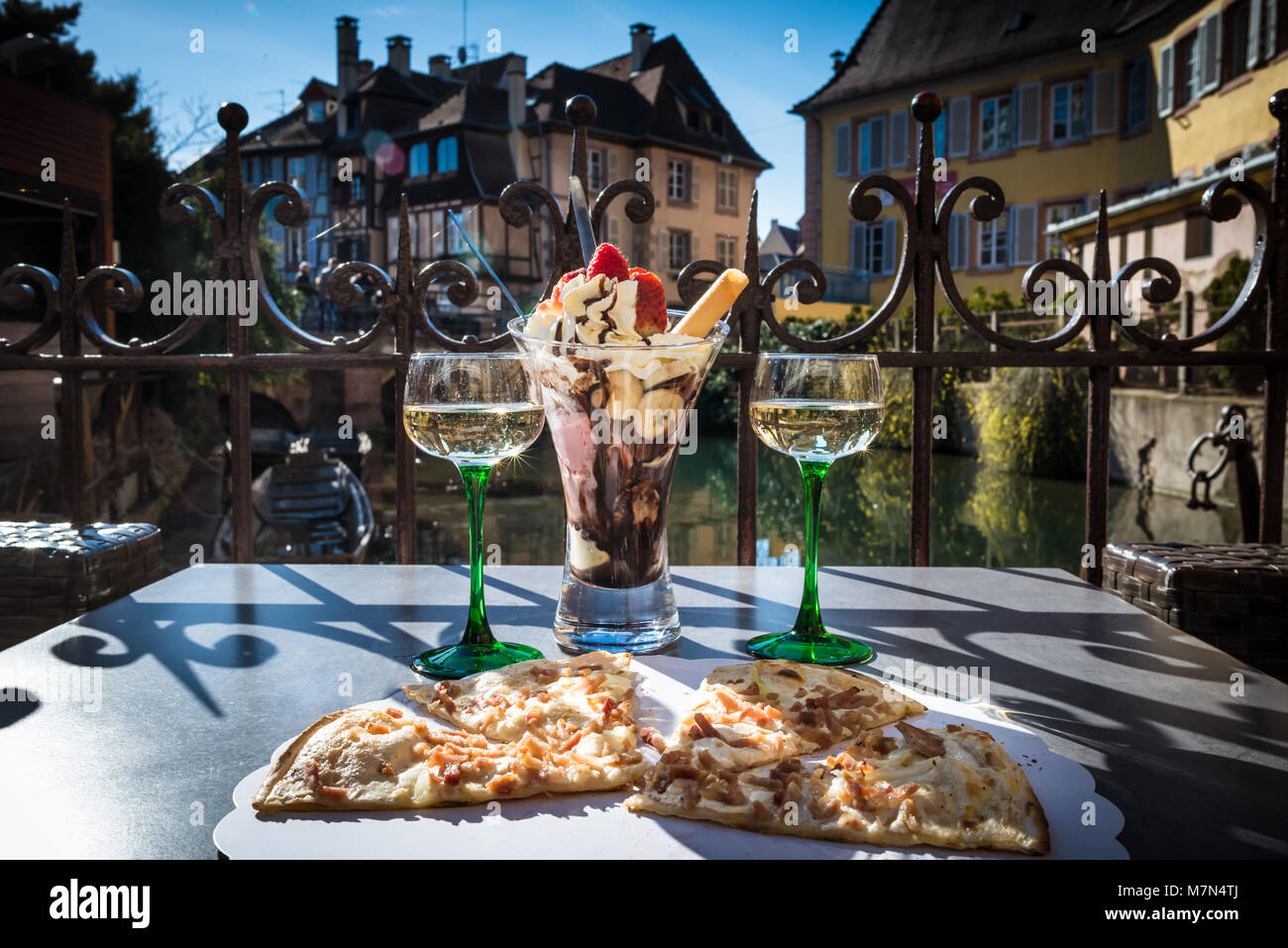 Traditionelle lokale Pizza mit Wein und Dessert in einem Cafe im Freien. Essen und Wein am Tisch auf der Terrasse mit schöner Aussicht auf den Fluss. Jahrgang Gebäude Stockfoto