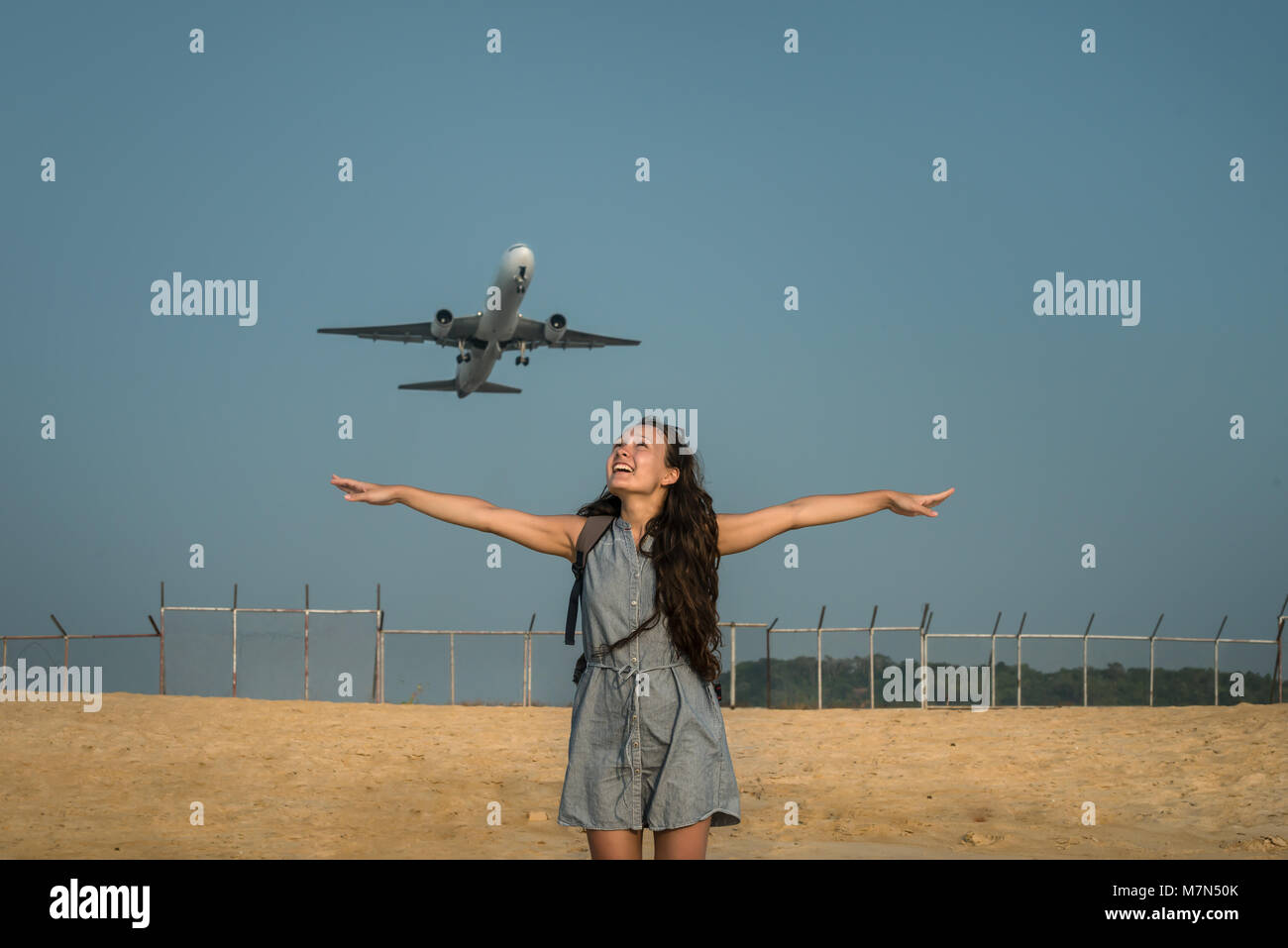 Flugzeug auf dem Hintergrund hinter einer jungen Frau. Weiblich steht und sich am Strand in der Nähe von Flughafen und breitete die Arme bereit für "Fly away". Stockfoto