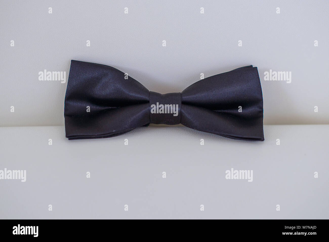 Seidig Bow Tie in dunkel blau oder Marine Farbe auf weißem Leder Sitzkissen mit weißem Hintergrund positioniert, elegante Accessoire für formale Kleidung Stockfoto