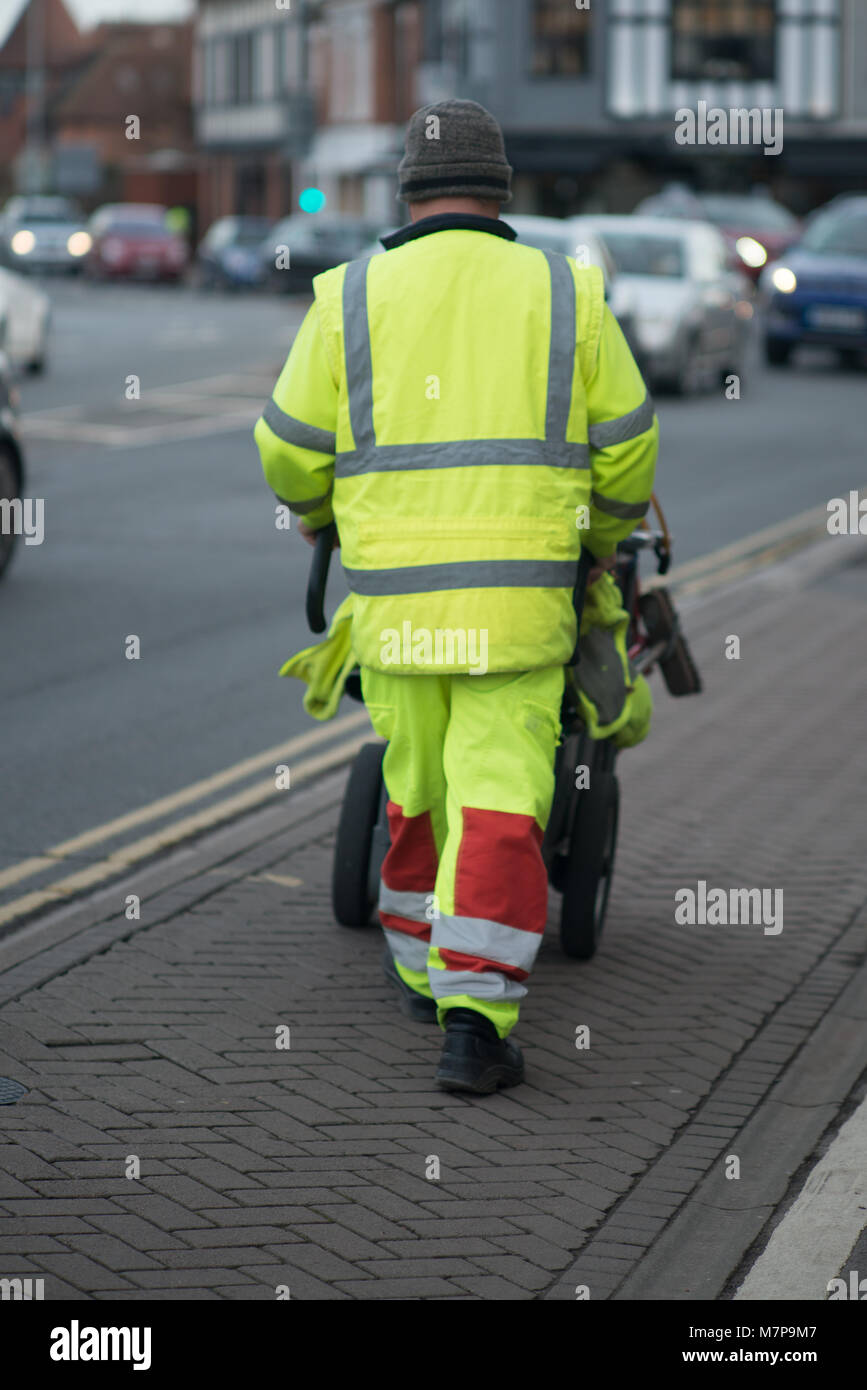 Street Sweeper geht weg drücken Ref und grau Barrow mit dem Gebäude im Hintergrund Stockfoto