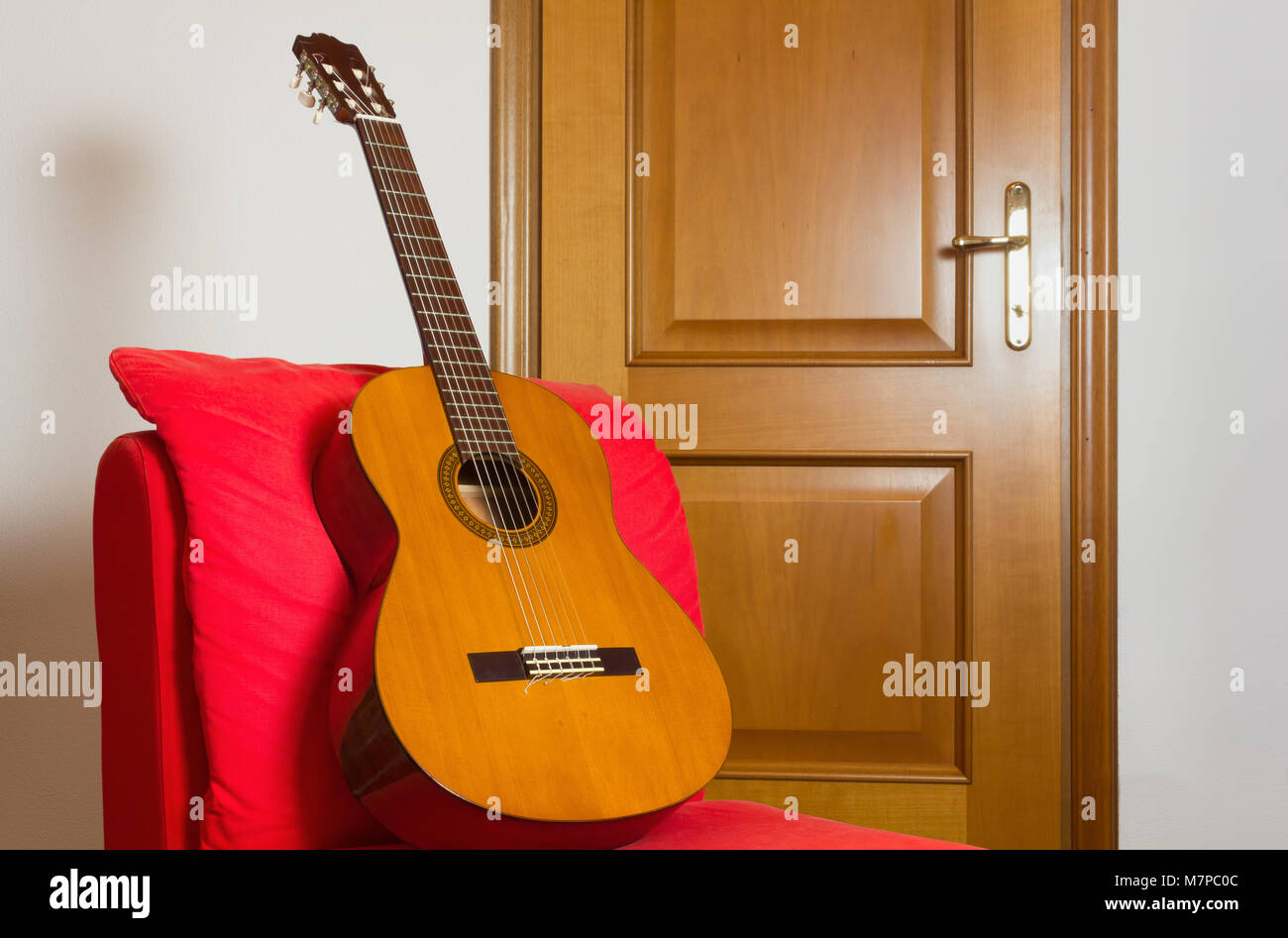 Klassische Gitarre auf einem roten Sessel mit einem hölzernen Tür im Hintergrund Stockfoto