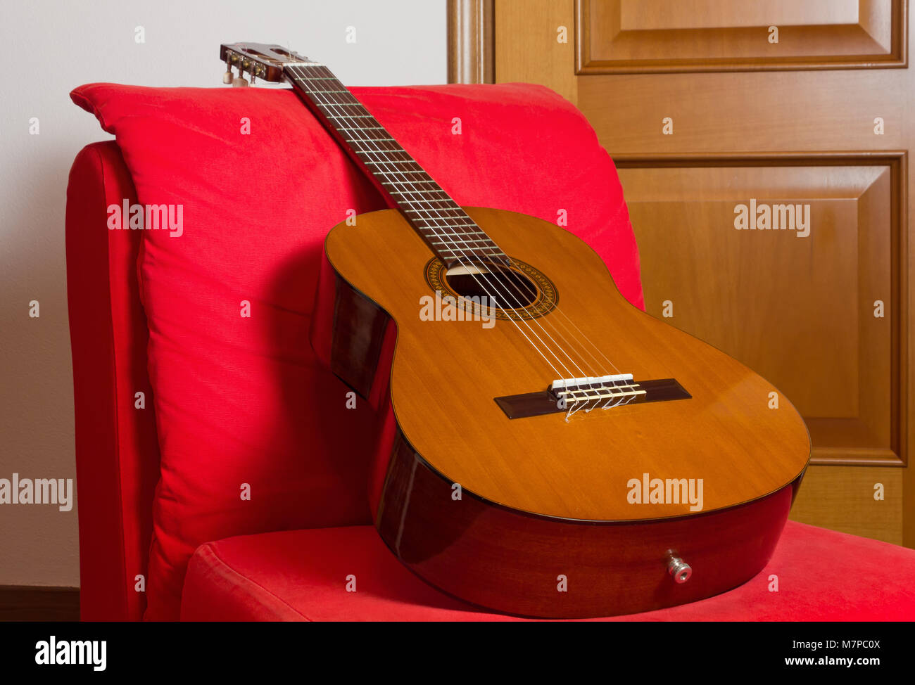 Klassische Gitarre auf einem roten Sessel mit einem hölzernen Tür im Hintergrund Stockfoto