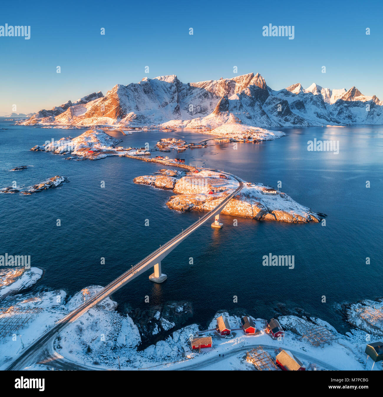 Luftaufnahme der Reine und Hamnoy bei Sonnenuntergang im Winter. Erstaunlich, Lofoten, Norwegen. Panoramablick auf die Landschaft und das blaue Meer, schneebedeckte Berge, Felsen, Villa Stockfoto