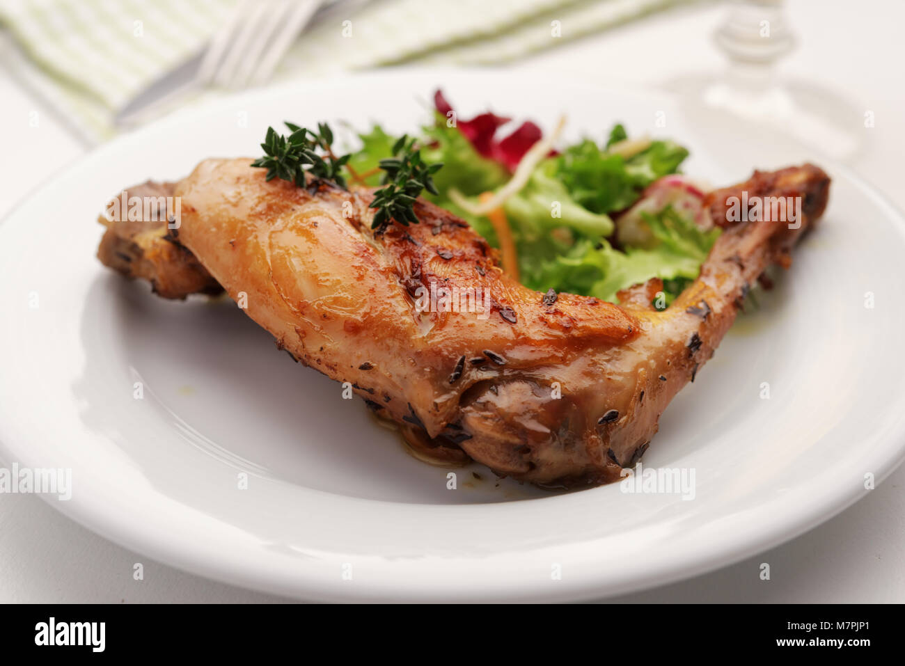 Gebratenes Kaninchen Bein mit Salat und Thymian auf einer Platte Stockfoto