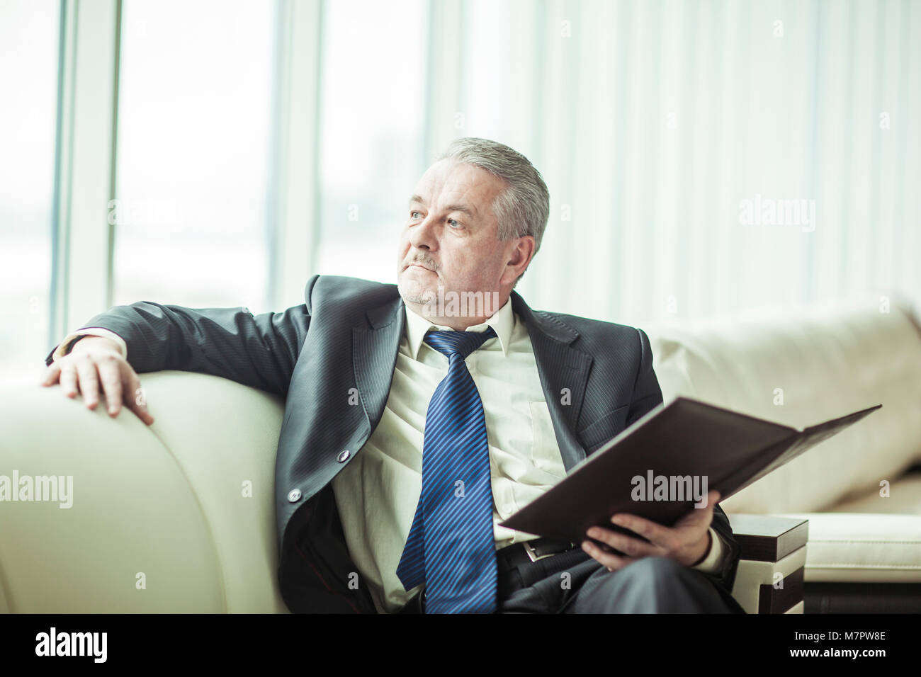 Erfolgreicher Geschäftsmann erwägt, einen neuen Vertrag auf dem Sofa sitzen im eigenen Büro Stockfoto