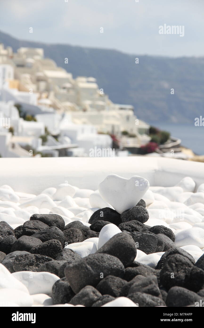 Zusammensetzung von schwarzen und weißen Steinen und ein Herz-form Stein mit Blick auf die Weißen wunderschönen Dorf Oia, Santorini, Kykladen, Griechenland. Stockfoto