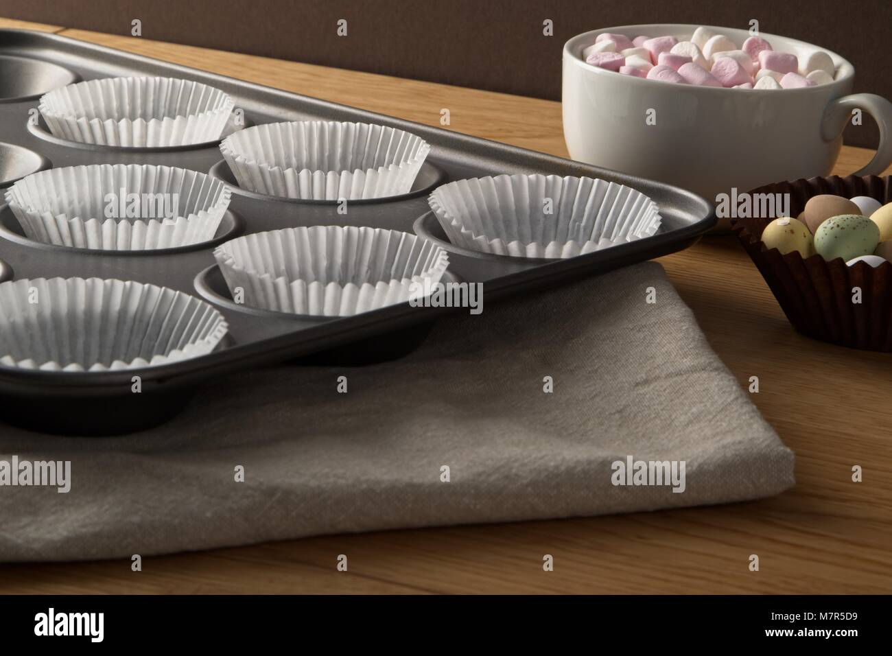 Cup Cake Tin mit Papier und Schokolade und Marshmallows Belag auf Eiche Oberfläche Stockfoto