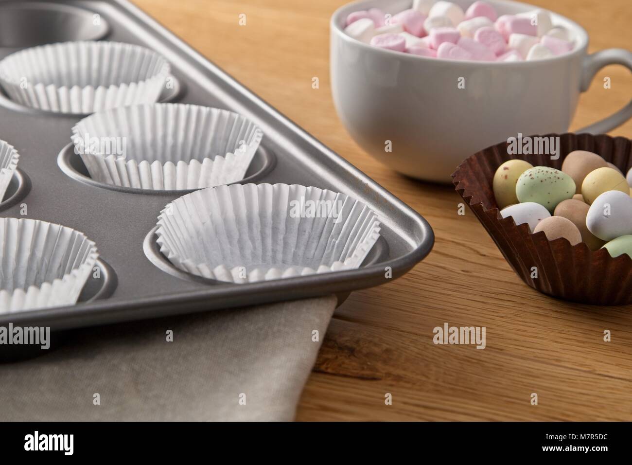 Cup Cake Tin mit Papier und Schokolade und Marshmallows Belag auf Eiche Oberfläche Stockfoto