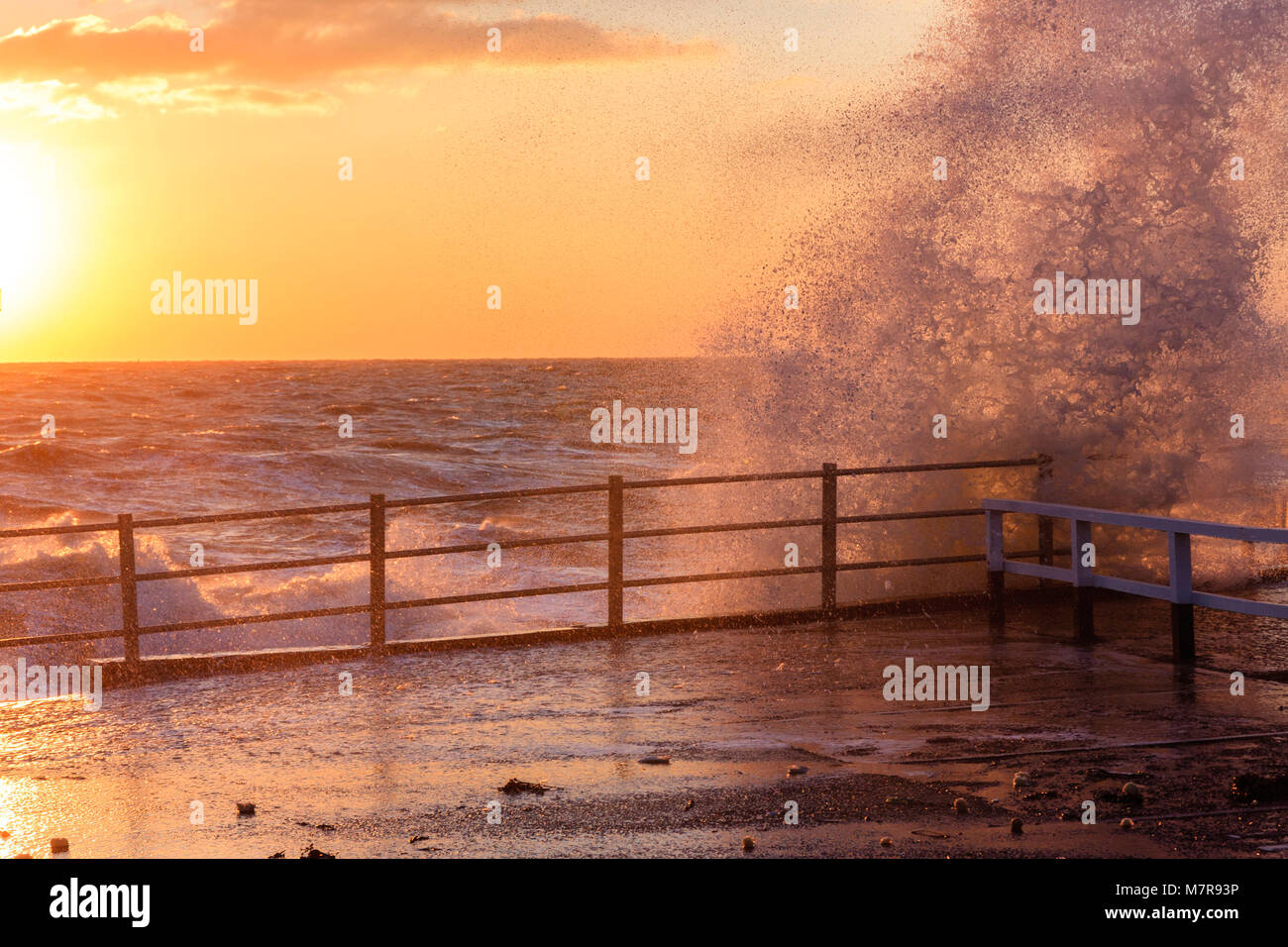 England, Broadstairs. Wellen, die über die hafenmauer bei Sonnenaufgang (unsichtbar). Sky orange und die Sonne abfackeln in die Seite des Bildes. Stockfoto