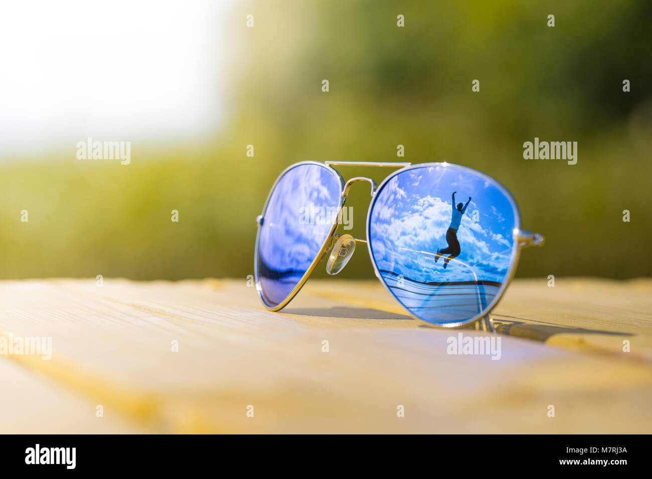 Ein fröhliches Mädchen, das in die Luft springt und sich in einer Sonnenbrille spiegelt Stockfoto