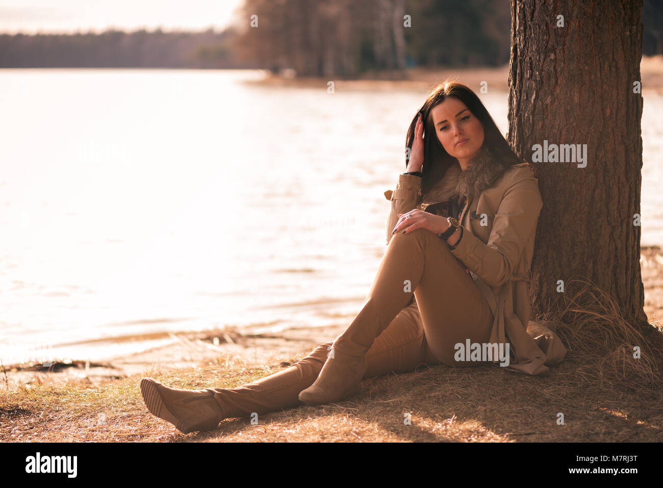 Brunette Mädchen sitzen unter dem Baum am See ufer Stockfoto