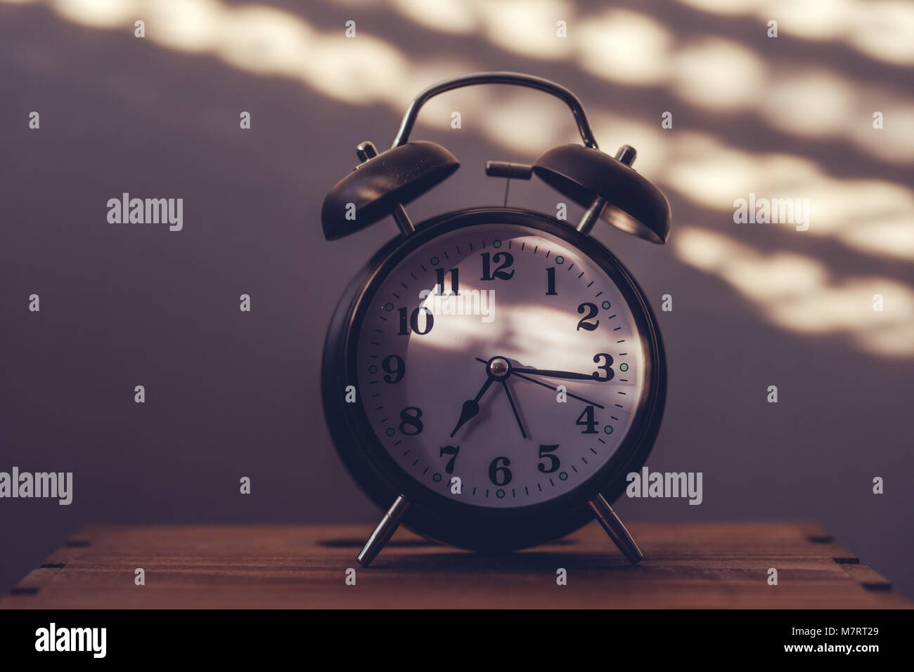 Wecker auf Nachttisch im Schlafzimmer tickende am frühen Morgen mit dem Sonnenlicht und Schatten an der Wand im Hintergrund Stockfoto