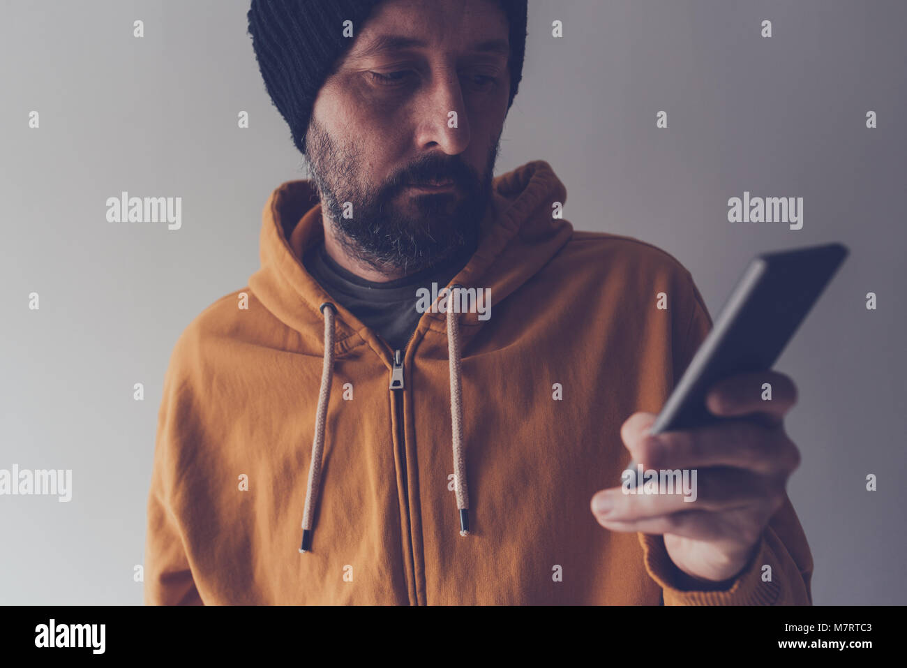 Casual erwachsenen Mann mit Kappe und gelben T-Shirt am Handy suchen, Low Key Kommunikation und Lifestyle Portrait mit selektiven Fokus Stockfoto