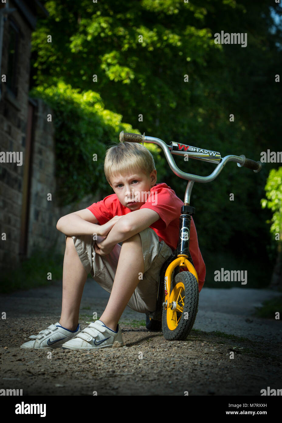 8 Jahre alter Junge saß auf einem Roller auf einem ländlichen Pfad Stockfoto