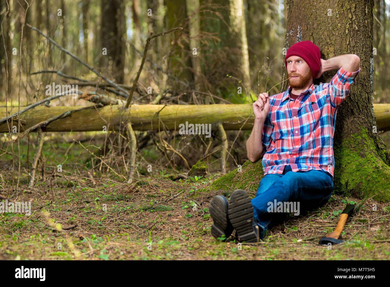 Holzfäller nach der Arbeit abschrecken, seine Axt und setzte sich unter einen Baum im Wald zu ruhen Stockfoto