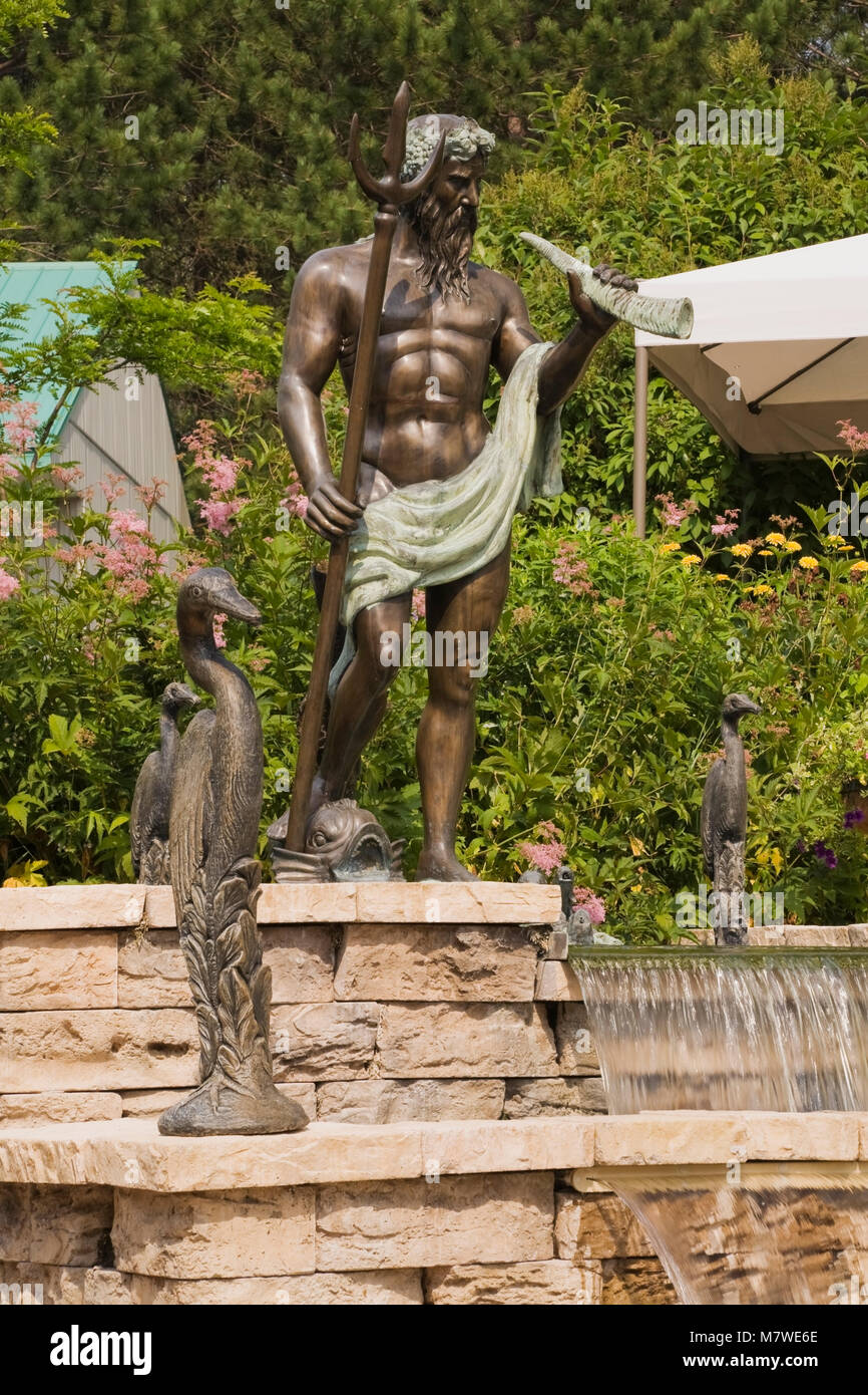 Beige cut-Mauer aus Stein und kaskadierende Springbrunnen und getönte Zement und Bronze griechischen Gott und Heron Skulpturen im privaten Garten Garten im Sommer Stockfoto