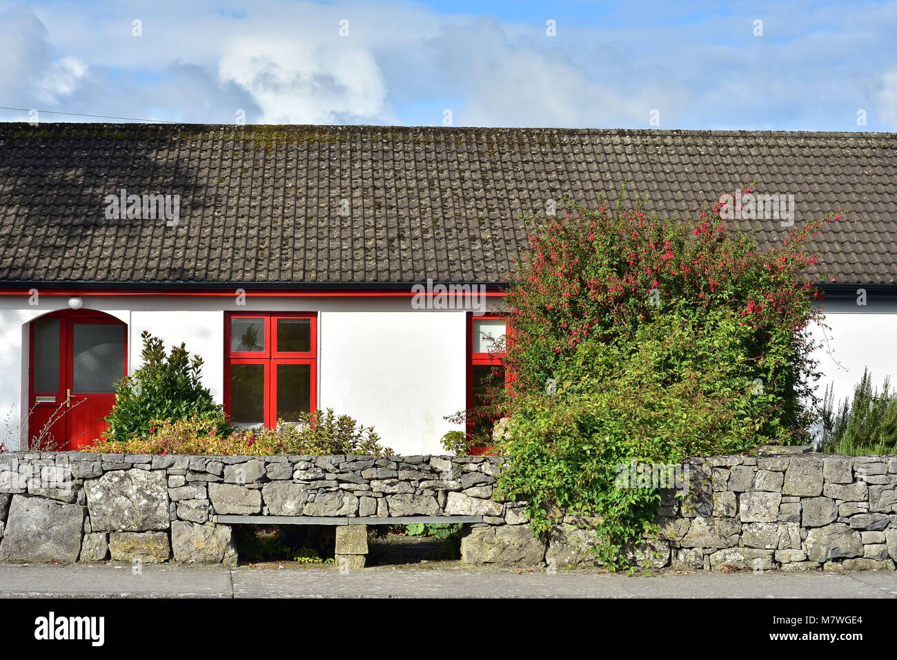 Irische Landschaft Haus mit hellen roten Tür- und Fensterrahmen hinter der niedrigen Mauer aus Stein. Stockfoto
