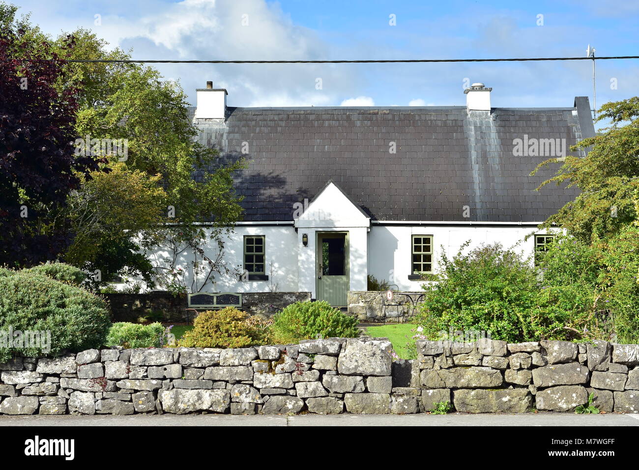White Irish Country Cottage mit hohem Dach auf Eigentum durch niedrige Steinmauer geschützt. Stockfoto