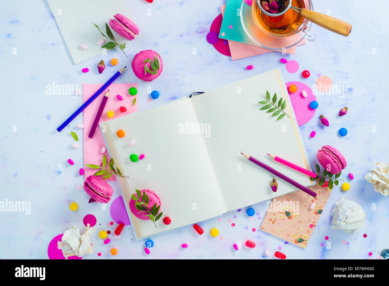 Bunte flach mit einem offenen Buch mit leeren Seiten, Konfetti, Süßigkeiten, Bonbons, rosa Umschlag, Makronen und Tee. Weibliche Schriftsteller Arbeitsplatz mit Stockfoto